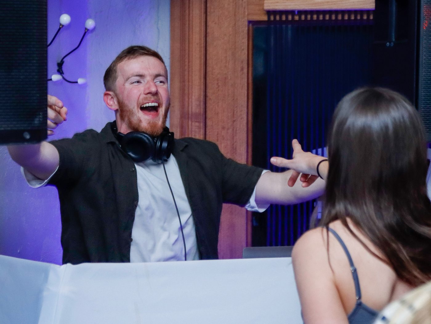 Tom reaching out to a guest while DJing at an indoor reception